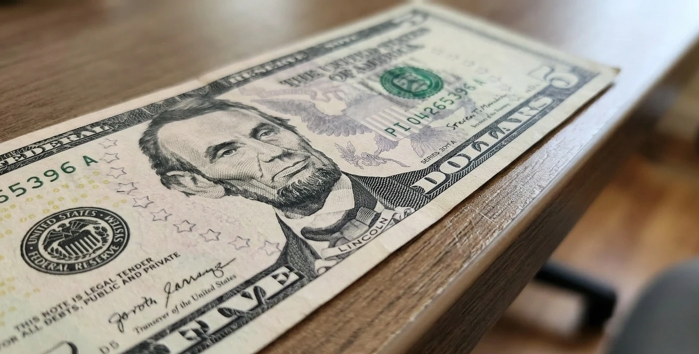 a 5 dollar bill placed near a blurred edge of a desk
